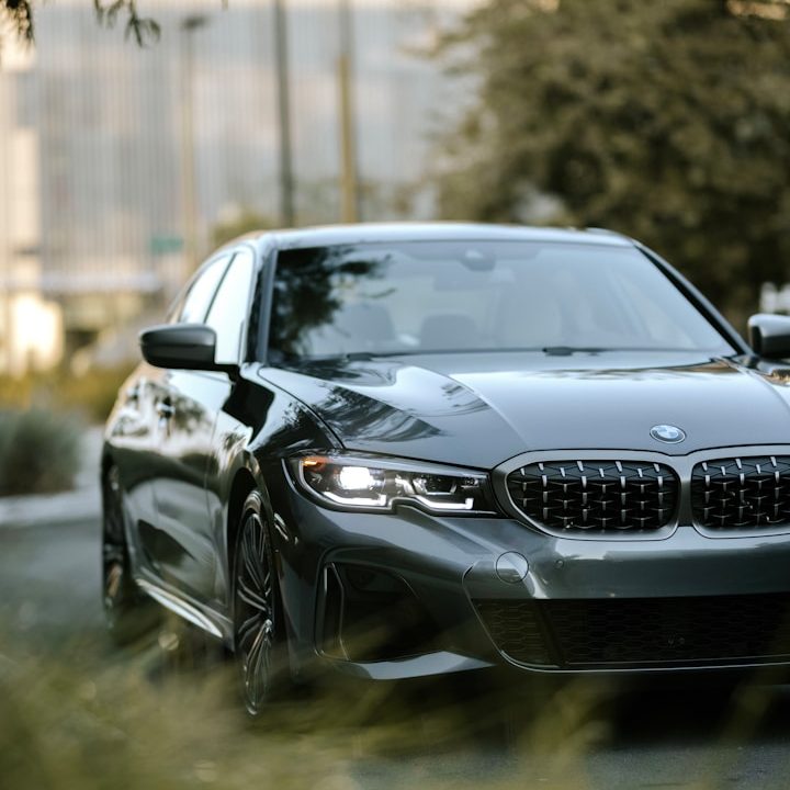 Ein schwarzer BMW fährt auf einer grünen, bewaldeten Straße.